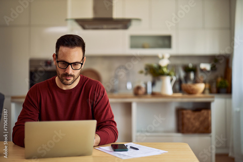 A focused freelance programmer with glasses typing on his laptop for his remote work project.