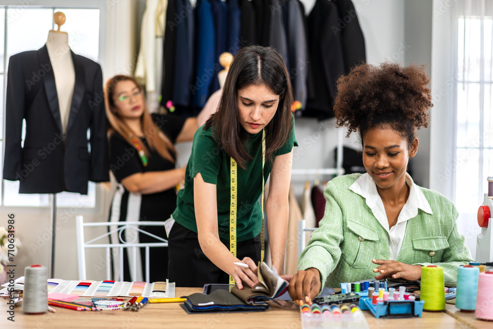 Fototapeta premium Portrait of young african american woman and young girl fashion designer stylish sitting and working with color samples.Attractive two designer girl work with colorful fabrics at fashion studio