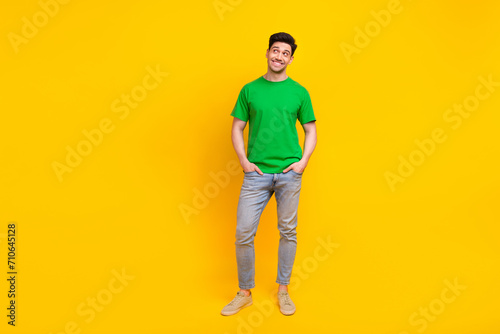 Full size photo of handsome guy wear stylish t-shirt arms in pockets look at discount empty space isolated on yellow color background