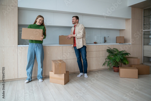 Joyful couple embraces start as move into new home, holding boxes with belongings, radiate happiness, anticipation. Wife and husband talking having fun enjoy life changes. Loving spouses relocating. photo