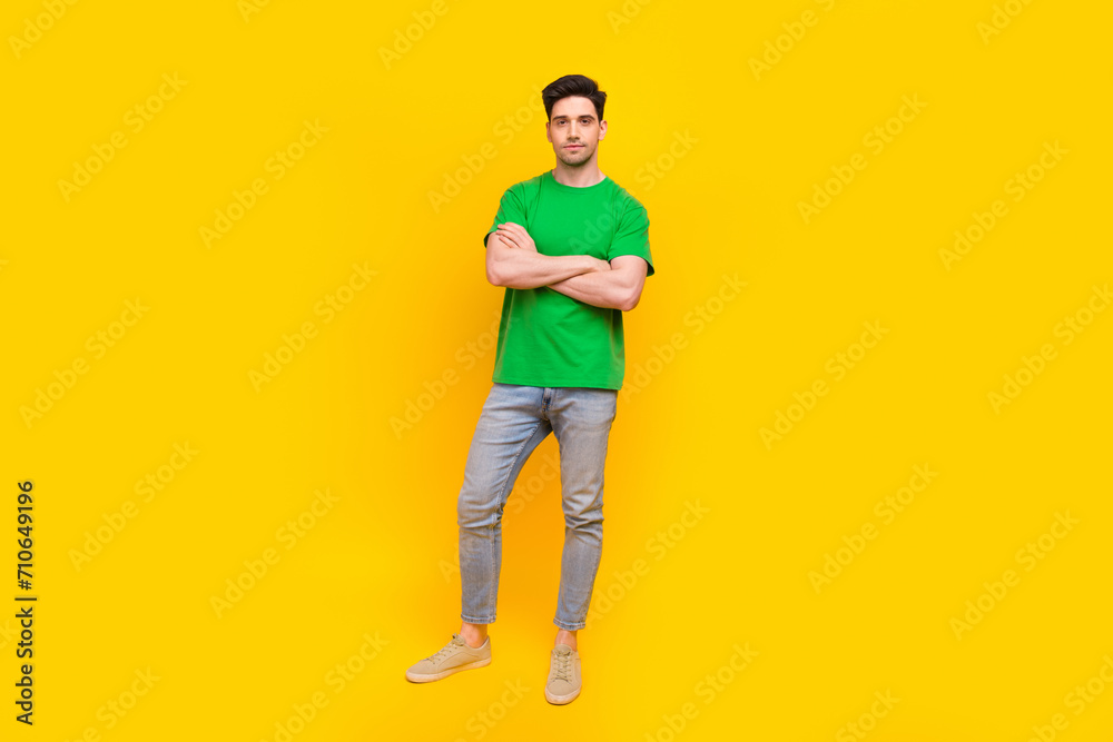 Fototapeta premium Full size photo of confident serious guy wear stylish t-shirt denim pants holding hands folded isolated on yellow color background
