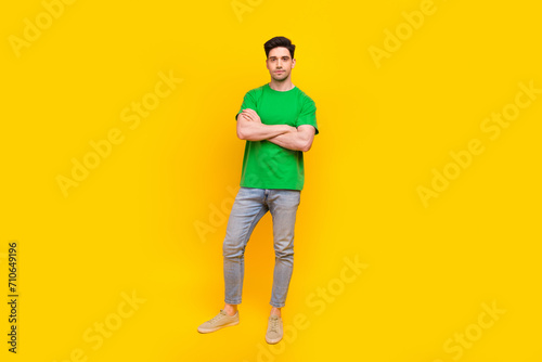 Full size photo of confident serious guy wear stylish t-shirt denim pants holding hands folded isolated on yellow color background