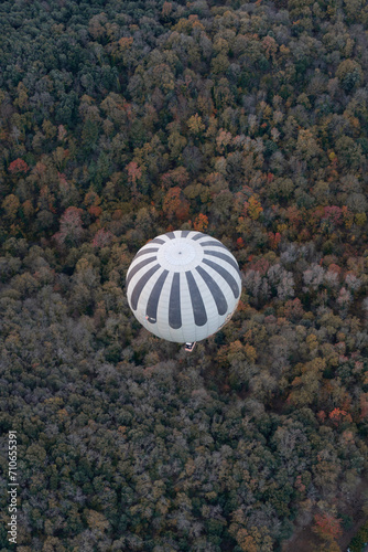 View from above of a hot air balloons flying over pinewood forest at La Garrotxa Volcanic Natural Park. Hot air balloon with black and white stripes with autumnal landscape in the background.