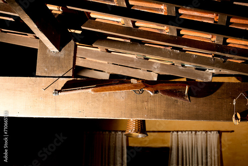Espingarda pendurada em uma viga de madeira de baixo de um telhado de telha de barro.  photo