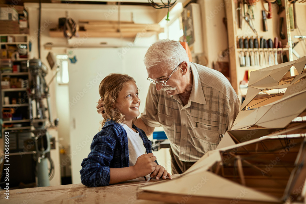 Grandfather and grandson working on a model boat in a woodworking workshop Grandfather and grandson working on a model boat in a woodworking workshop