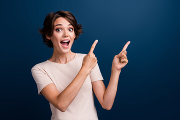 Portrait of funny amazed girl promoter directing fingers empty blank space cool news open mouth isolated dark blue color background