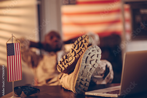 Relaxed soldier with feet on desk next to American flag and laptop