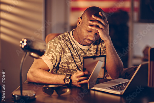 Stressed military man looking at photo while working late on laptop photo