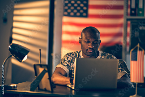 Young American soldier working on laptop at army base photo