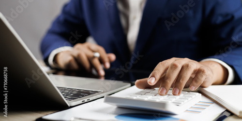 Businessman calculating taxes and finances on laptop at corporate desk, Financial success, Accountant working with calculator and paperwork ,Economy concept. Man managing budget and market statistics.