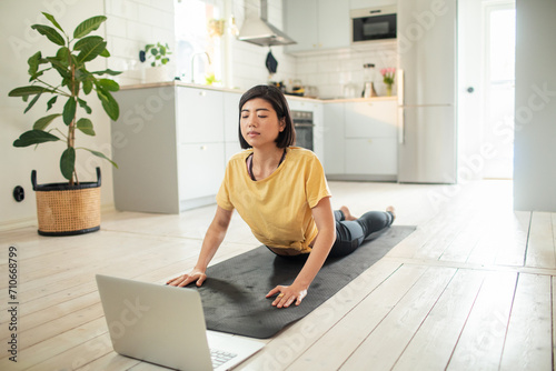 Young adult woman doing yoga with laptop at home photo