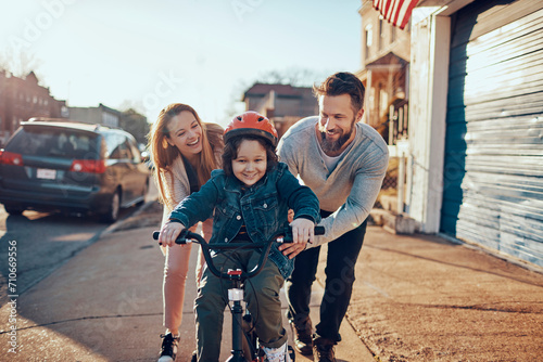 Family teaching child to ride bicycle in suburban neighborhood