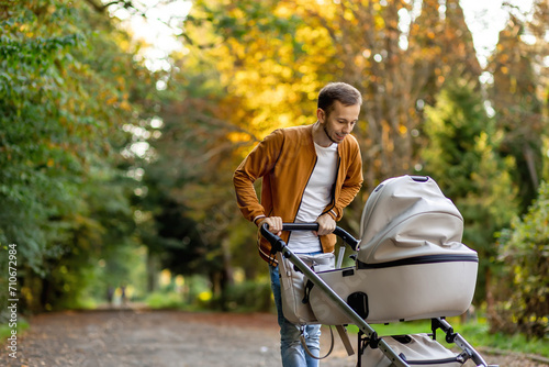 happy father pushing infant baby stroller and walking in the park. Spending time with newborn and breathing fresh air. photo