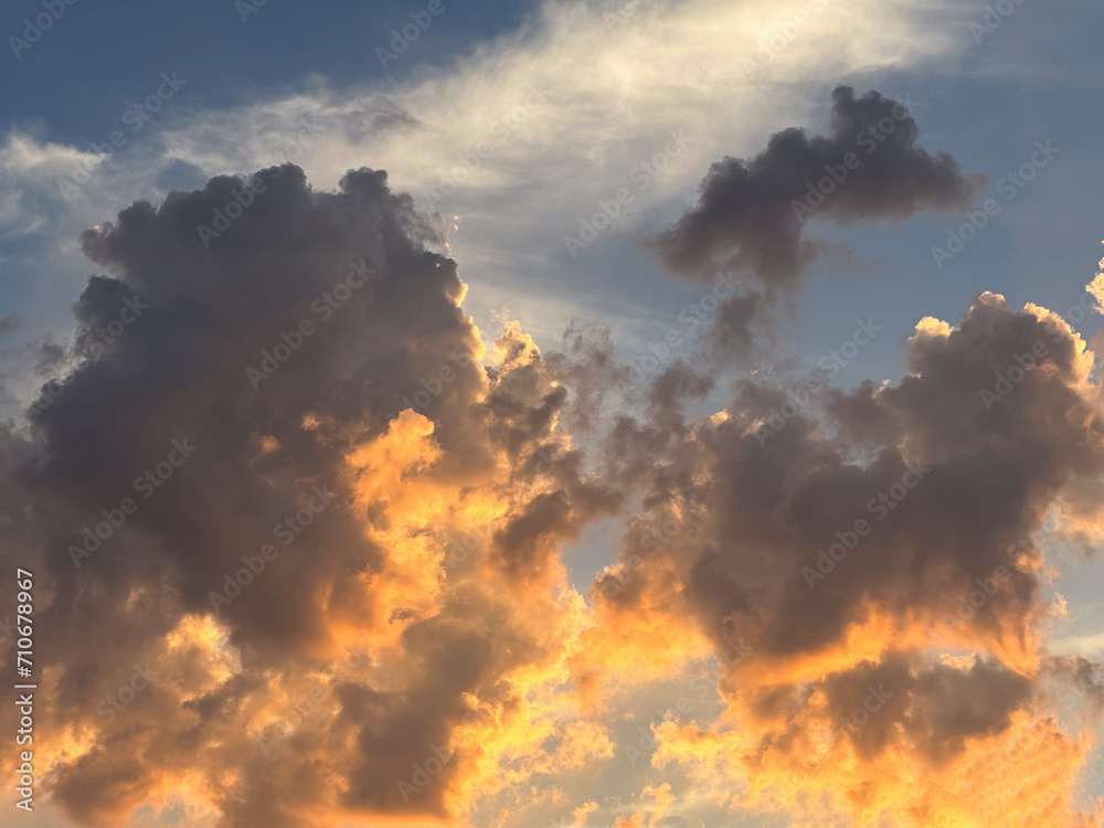 A vibrant sunset casts a warm orange glow on unique cloud formations, creating a striking contrast with the remaining patches of blue sky.