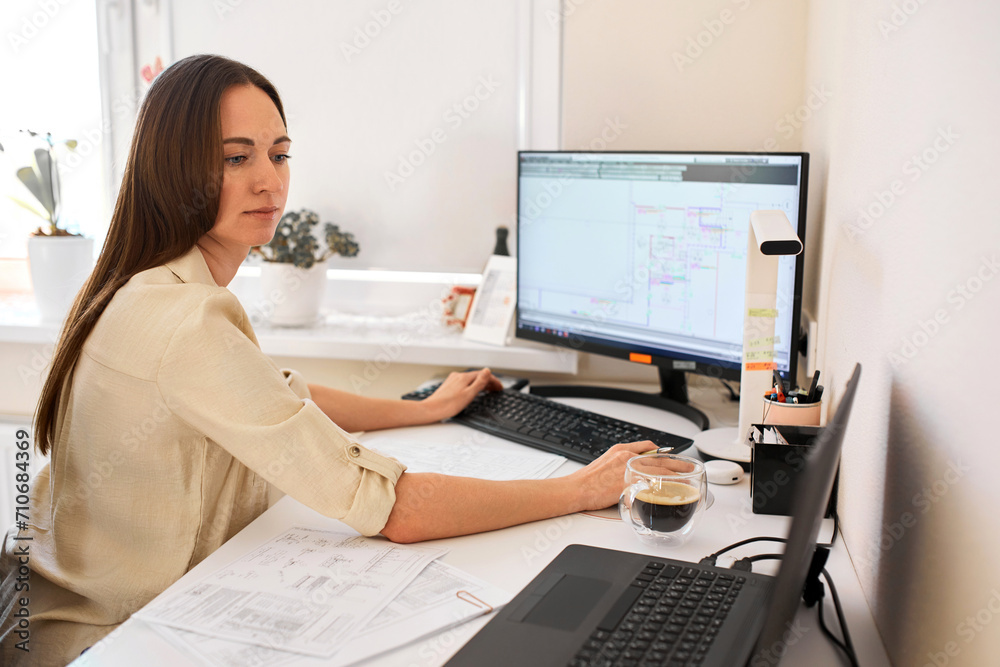 Portrait of a remote worker. An adult woman sits at a table in front of a computer and draws up a costly estimate. Confident young lady freelancer working from home. Portrait of a remote worker. An adult woman sits at a table in front of a computer and draws up a costly estimate. Confident young lady freelancer working from home.