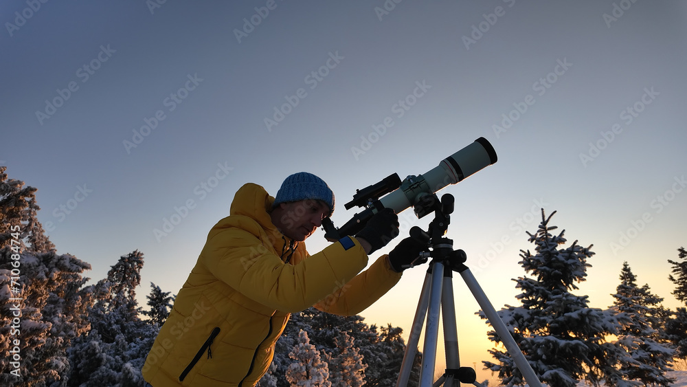 Amateur astronomer looking at the skies with a telescope in winter time.