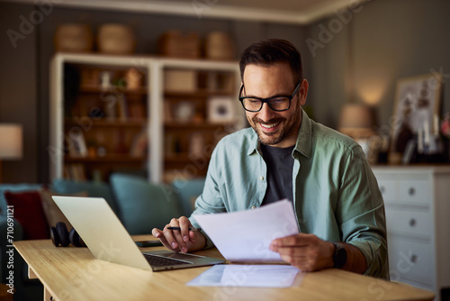 A smiling male college professor reading a student's essay paper in his office in front of a laptop. photo