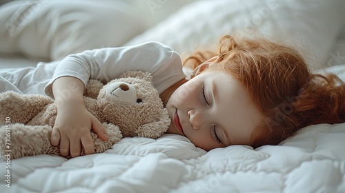 Little girl with red hair sleeps on the bed and hugs her favorite cozy soft toy, smiling in her sleep. Happy childhood 