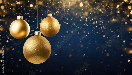 three golden christmas baubles hanging against the dark blue background with golden dust new year banner