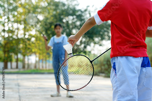 Asian girl and boy play badminton outdoors at the park together on vacation. Soft and selective focus.
