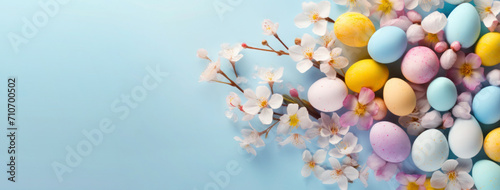 Colorful Easter eggs with spring blossom flowers on light blue background. Banner with copy space. Top view