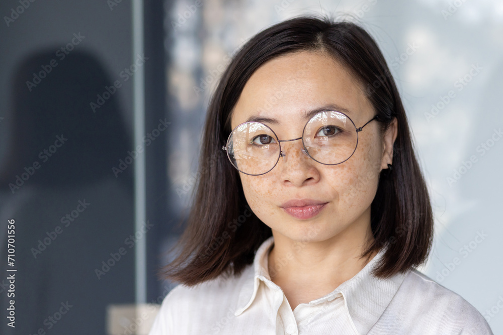 Portrait of a young Asian businesswoman with glasses, exuding confidence and professionalism at her office desk. Portrait of a young Asian businesswoman with glasses, exuding confidence and professionalism at her office desk.