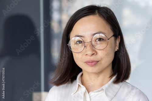 Portrait of a young Asian businesswoman with glasses, exuding confidence and professionalism at her office desk.
