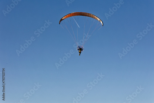 Motorized paraglider flying against the blue sky with clouds, outdoor activity, extreme sports, extreme sports, paraglider flying in the sun in the sky. The sport of paragliding