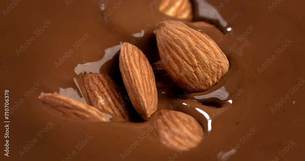 Super slow motion macro of bio organic almond nuts falling in creamy melted liquid dark cocoa chocolate with splashing dripping drops at 1000 fps.