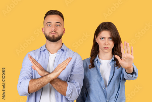 Man and woman gesturing stop, showing denial or refusal on yellow background