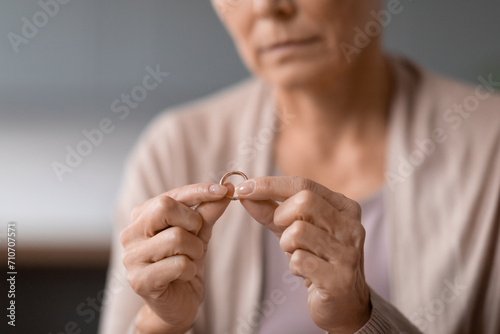 Unhappy unrecognizable senior widow woman holding wedding ring indoors, cropped photo