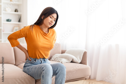 Unhappy chinese woman have back pain after nap on couch photo