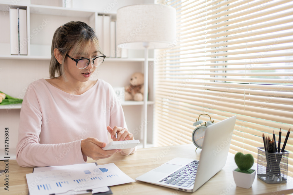 Young Businesswoman presses a calculator to calculate income tax and corporate income in a private office, Statistical graphs of investing in real estate, Finance, Accounting, Tex, Work for home. Young Businesswoman presses a calculator to calculate income tax and corporate income in a private office, Statistical graphs of investing in real estate, Finance, Accounting, Tex, Work for home.