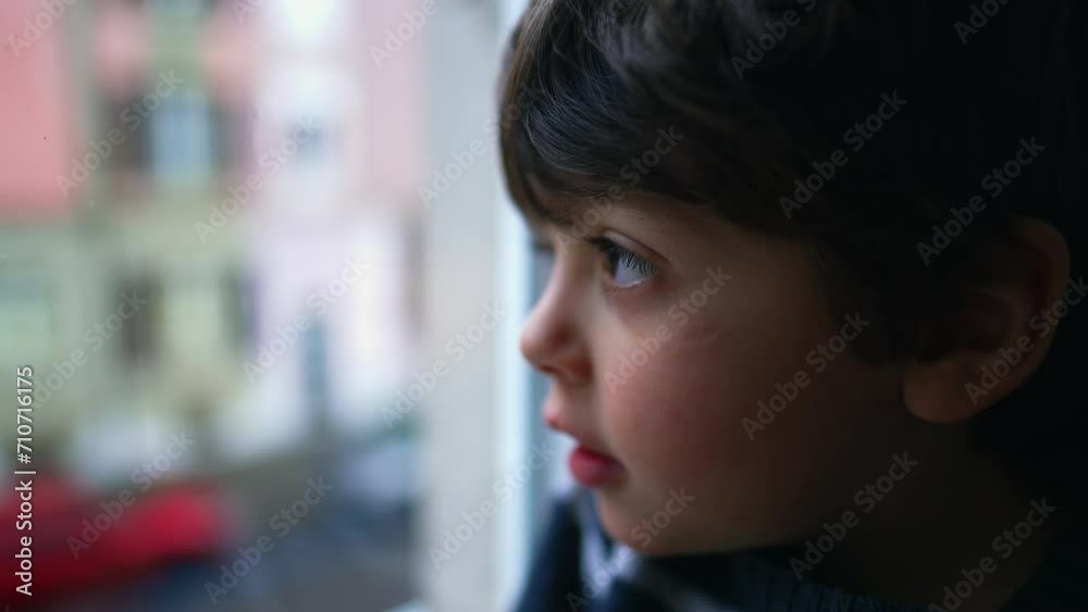 Profile face close-up of little boy staring at window from home. Child looks out confined in residence Profile face close-up of little boy staring at window from home. Child looks out confined in residence