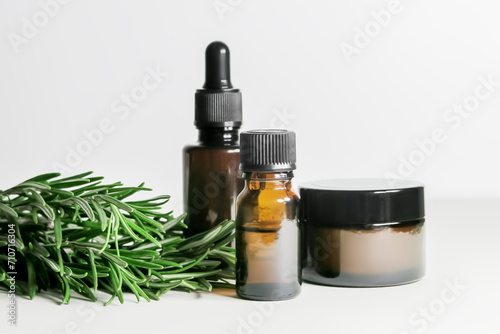 glass bottles and jar with rosemary essential oil and branches of fresh rosemary on a white background
