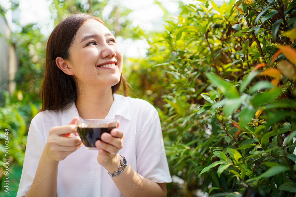 Asian beautiful woman enjoy drinking a cup of coffee in morning at home backyard. Smiling cheerful woman drinks a black coffee in the nature close up. Asian beautiful woman enjoy drinking a cup of coffee in morning at home backyard. Smiling cheerful woman drinks a black coffee in the nature close up.