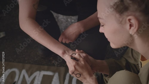 Young Caucasian woman drawing feminist sign on wrist of her female co-worker while getting ready for protest strike at industrial plantYoung Caucasian woman drawing feminist sign on wrist of her femal photo