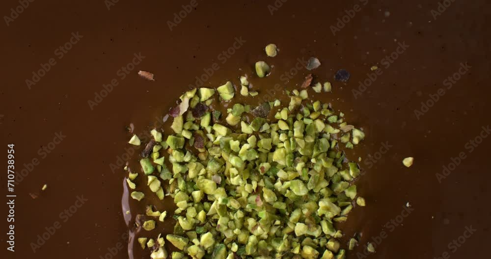 Super slow motion macro of bio organic pistachio grains falling in creamy melted liquid dark cocoa chocolate with splashing dripping drops at 1000 fps.