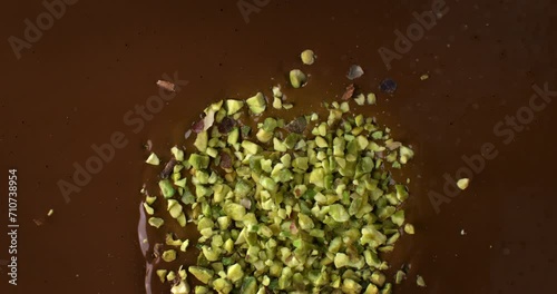 Super slow motion macro of bio organic pistachio grains falling in creamy melted liquid dark cocoa chocolate with splashing dripping drops at 1000 fps.