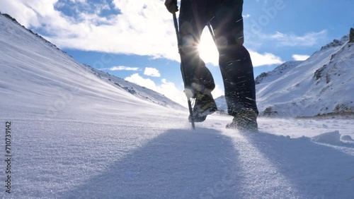 A tourist travels through the mountains in winter on a windy but sunny day. Man with backpack and trekking poles. Slow Motion 2x