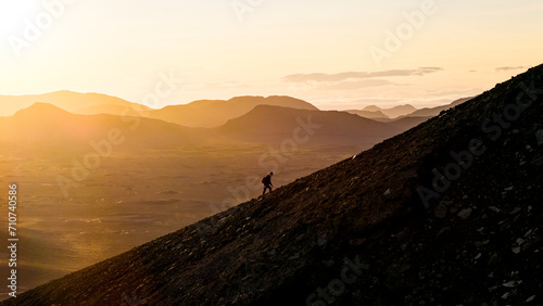 Aerial drone view of a silhouette person walking uphill on Blahylur Crater during sunset in the highlands of Iceland. photo