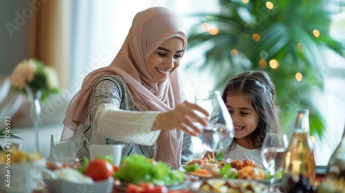 Happy Muslim mother pours water into daughter's glass during family meal at home.