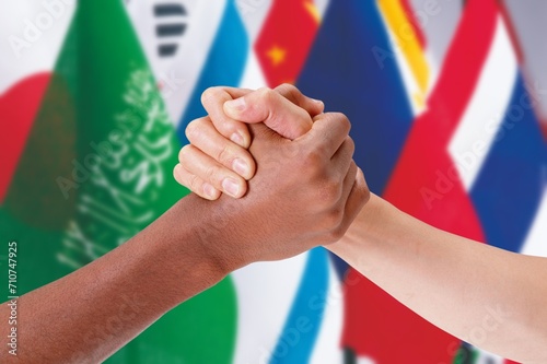 Hands of people of different ethicity clutching against the background of flags. Concept of relation, diversity, inclusion, community, togetherness.