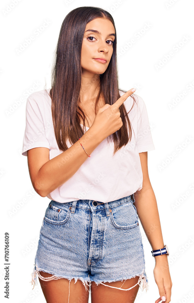 Fototapeta premium Young hispanic woman wearing casual white tshirt pointing with hand finger to the side showing advertisement, serious and calm face