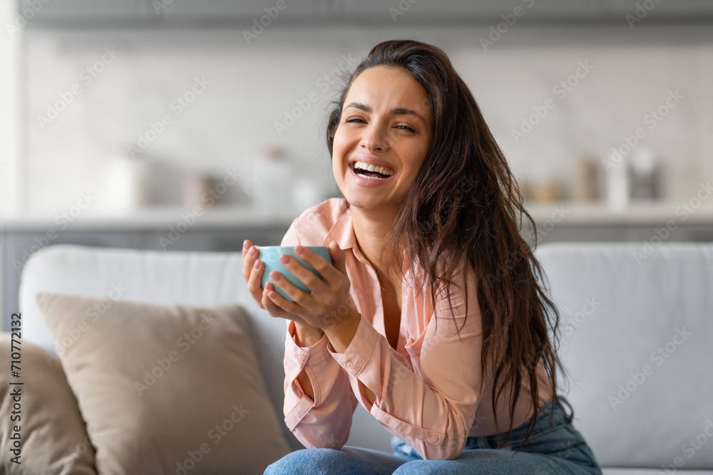 Joyful woman laughing while holding cup, in cozy home setting Joyful woman laughing while holding cup, in cozy home setting