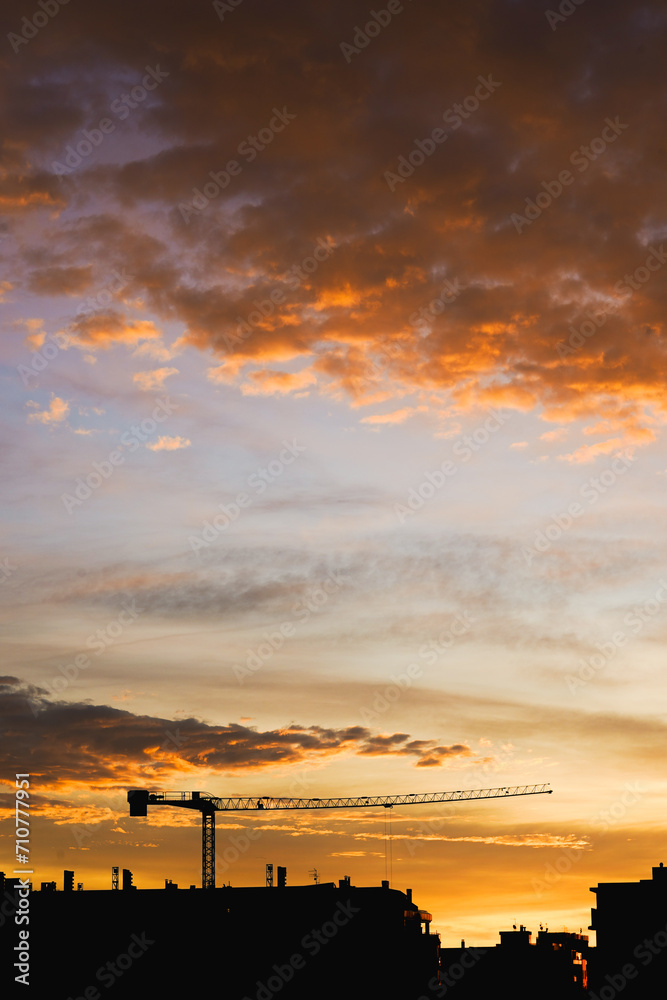  Majestic sunset with a silhouette of a construction crane over a city.
