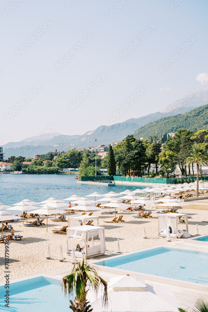 Sandy beach with swimming pools, sun loungers and sun umbrellas on the seashore