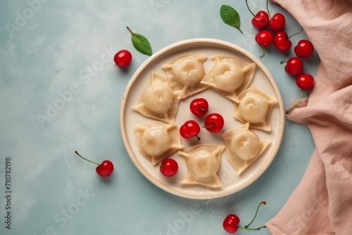 A stack of dumplings with cherries laid out on a pink plate located on a blue background. Fresh cherries accentuate the filling. Copy space banner Concept: traditional sweet dish made from dough.
