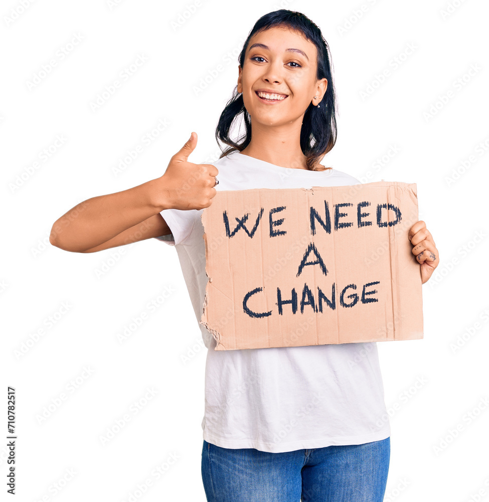Young woman holding we need a change banner smiling happy and positive, thumb up doing excellent and approval sign Young woman holding we need a change banner smiling happy and positive, thumb up doing excellent and approval sign