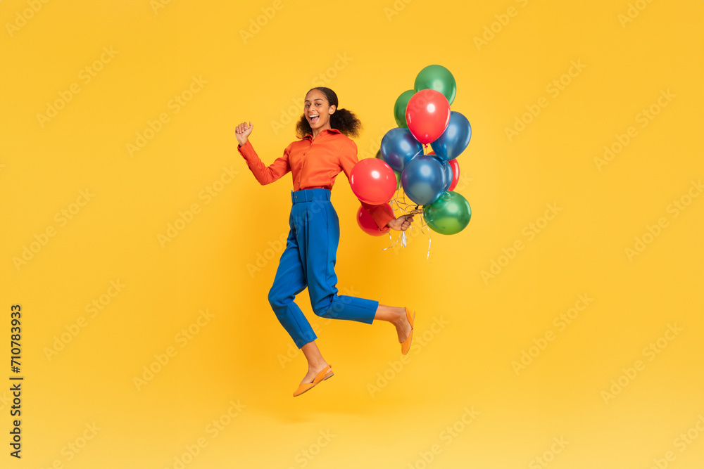 Cheerful black teen girl jumping with bunch of balloons, studio